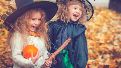 Two children in the woods with pumpkin, broomstick and dressed at witches